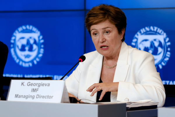 Kristalina Georgieva, IMF Managing Director, speaking at a press conference with a microphone, seated at a table with a nameplate, against a blue IMF backdrop.